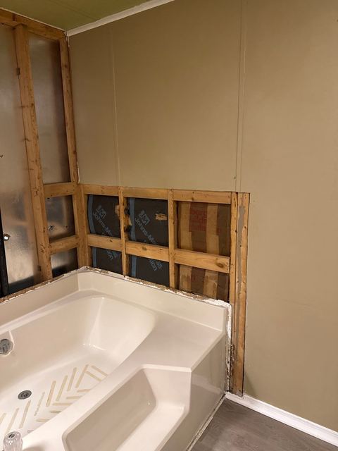 Water-damaged drywall cut open beside a bathtub, and the tub wall stripped to clean studs.